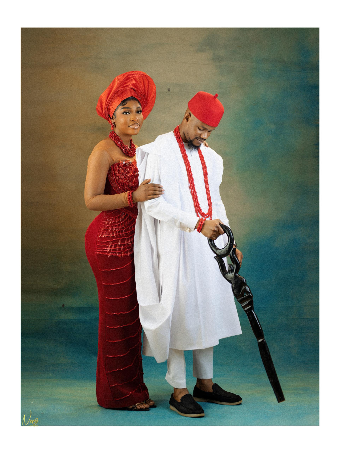 Kent and Iheoma standing close together in traditional attire with a carved staff